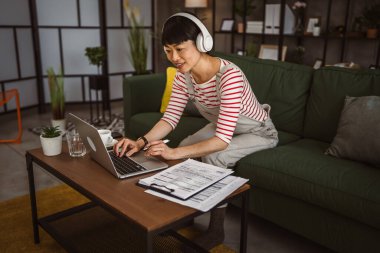 Japon kadın evde dizüstü bilgisayarda çalışıyor ve belgeyi tutuyor