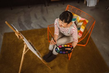 Bir kadın sanatçı evde boya fırçasıyla resim yapıyor.