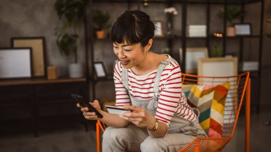 Gözlüklü Japon kadın sandalyeye oturur kredi kartı ve cep telefonunu evde online alışveriş yaparak kullanır.