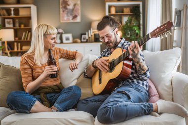 Yetişkin çiftler evde gitar çalıp birlikte mutlu bira içerler.