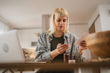 Genç beyaz kadın evdeki mutfakta tıp ve internet için talimat tarifi okuyor.