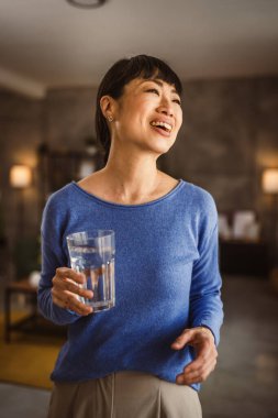 Evde bir bardak suyla Japon olgun bir kadının portresi.