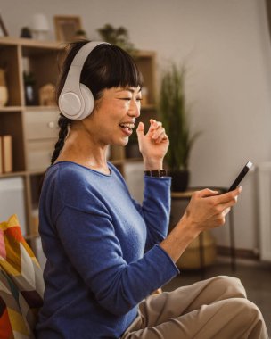 Kulaklıklı olgun Japon kadın cep telefonuyla müzik dinliyor.