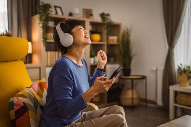 Kulaklıklı olgun Japon kadın cep telefonuyla müzik dinliyor.