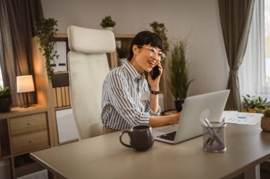 Gözlüklü olgun Japon kadın ofiste telefonla konuşuyor.