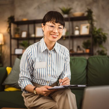 Olgun Japon kadın, not panosunu tut ve evden çalışırken dizüstü bilgisayara bak.