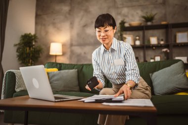 Gözlüklü olgun Japon kadın cep telefonunu tutuyor ve evrak işlerini evden yapıyor.