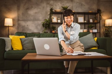 Gözlüklü olgun Japon kadın evde çalışıyor ve telefonda birden fazla iş yapıyor.