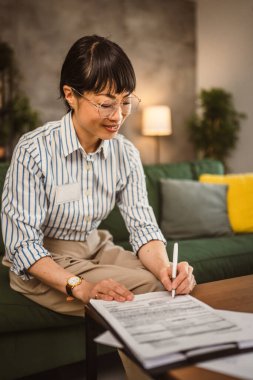 Gözlüklü olgun Japon kadın evden çalışıyor ve belge imzalıyor.