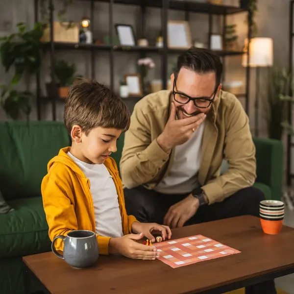 眼鏡と息子の慎重な遊びボードゲームと一緒に自宅で楽しい ストックフォト