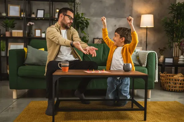 眼鏡と息子の慎重な遊びボードゲームと父親は彼が負けている怒っている原因 ストック写真