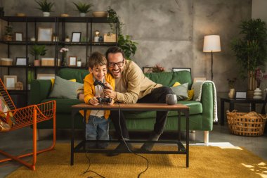 Baba ve oğlu beyaz tenli, joystick ile video oyunu oynuyor ve evde eğleniyor.