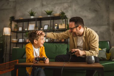 Baba ve oğlu beyaz tenli, joystick ile video oyunu oynuyor ve evde eğleniyor.