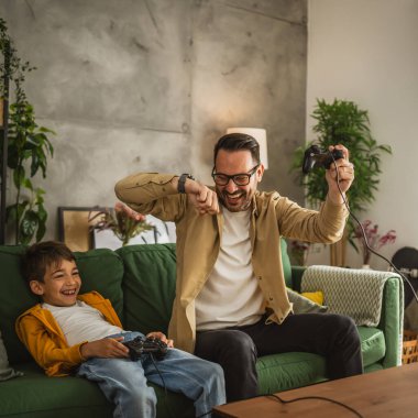 Baba ve oğlu beyaz tenli, joystick ile video oyunu oynuyor ve evde eğleniyor.