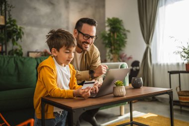 Baba ve oğlu Kafkasyalılar evdeki bilgisayarlarında kredi kartıyla online alışveriş yapıyorlar.