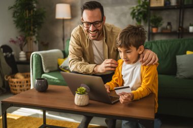 Baba ve oğlu Kafkasyalılar evdeki bilgisayarlarında kredi kartıyla online alışveriş yapıyorlar.