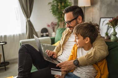 Baba ve oğlu Kafkasyalılar evdeki bilgisayarlarında kredi kartıyla online alışveriş yapıyorlar.