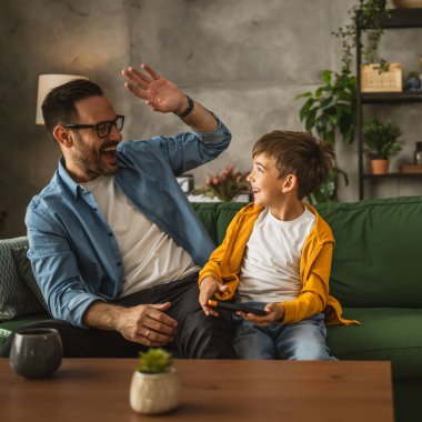 Baba ve oğul cep telefonuyla video oyunu oynuyor ve evde eğleniyorlar.