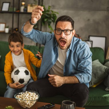 Baba ve oğlu Kafkas futbol maçı izleyip evde tezahürat yapıyorlar. Gürültülü, heyecanlı, mutlu.