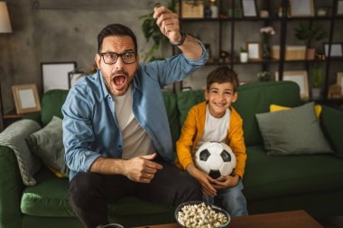 Baba ve oğlu Kafkas futbol maçı izleyip evde tezahürat yapıyorlar. Gürültülü, heyecanlı, mutlu.