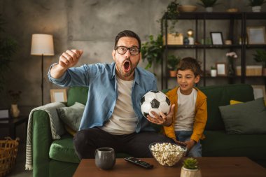 Baba ve oğlu Kafkas futbol maçı izleyip evde tezahürat yapıyorlar. Gürültülü, heyecanlı, mutlu.