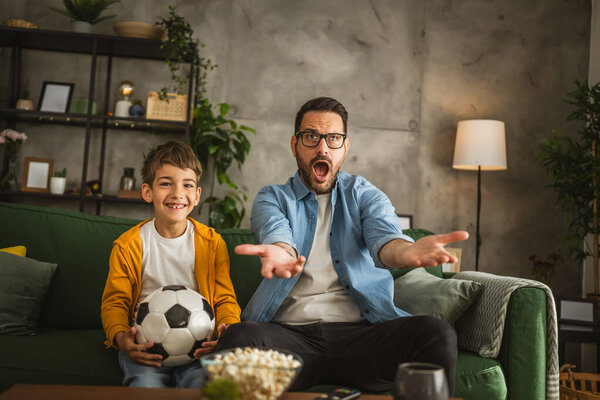 Father and son caucasian watch football match and cheer at home noisy, excited, happy