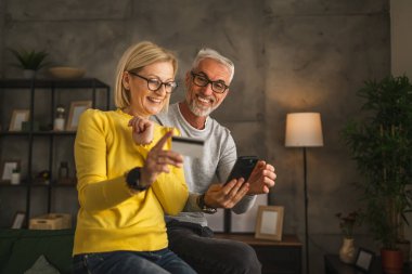 Olgun ya da yaşlı Kafkasyalı karı-koca internetten alışveriş yapıyor. Evde oturan koca cep telefonunu tutuyor ve kredi kartından bilgi okuyor.