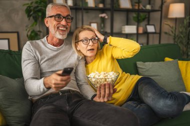 Olgun yaşlı çift karı koca korku filmi izler ve evde uzaktan kumandayla patlamış mısır tutarlar.