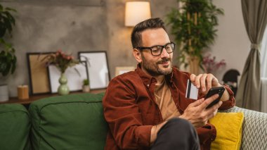 İnternette cep telefonuyla alışveriş yapan yetişkinlerin portresi ve evde kredi kartı bulundurmak.