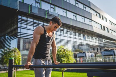 Açık spor salonunda antrenman yapan genç bir beyaz erkek sporcu yaz günü şehirde sağlıklı yaşam tarzı ve dinlenme eğitimi kavramını geliştirir.