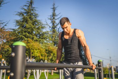 Açık spor salonunda antrenman yapan genç bir beyaz erkek sporcu yaz günü şehirde sağlıklı yaşam tarzı ve dinlenme eğitimi kavramını geliştirir.