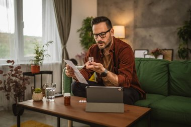 Yetişkin Kafkasyalı bir adam kanepeye oturur ve evde tıp tarifi okur.