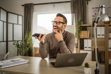 Yetişkin adam bilgisayarda çalışır ve ofisteki sesli mesaj veya sesli mesajları kaydeder.