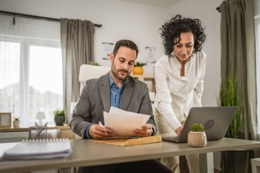 İki iş arkadaşı ofiste dizüstü bilgisayarda birlikte çalışıyorlar.