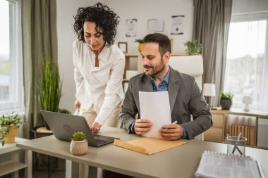 İki iş arkadaşı ofiste dizüstü bilgisayarda birlikte çalışıyorlar.
