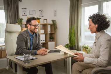 Olgun bir kadın ofiste oturup müdürle ya da patronla iş görüşmesi yapar.