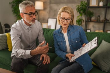 Olgun yaşlı kadın, kocaya evdeki evrakların nerede imzalanacağını gösterir.