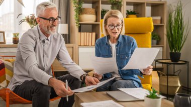 Olgun yaşlı çift karı koca birlikte çalışırlar. Evlerinde birlikte çalışırlar. Erkek ve kadın belgelere bakar ve konuşurlar.