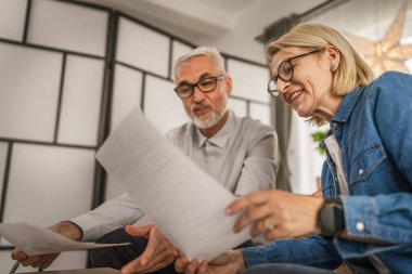 Olgun yaşlı çift karı koca birlikte çalışırlar. Evlerinde birlikte çalışırlar. Erkek ve kadın belgelere bakar ve konuşurlar.
