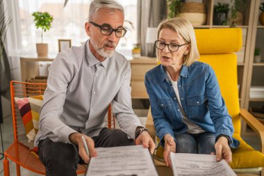 Olgun yaşlı çift karı koca birlikte çalışırlar. Evlerinde birlikte çalışırlar. Erkek ve kadın belgelere bakar ve konuşurlar.