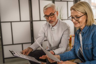 Olgun yaşlı çift karı koca birlikte çalışırlar. Evlerinde birlikte çalışırlar. Erkek ve kadın belgelere bakar ve konuşurlar.