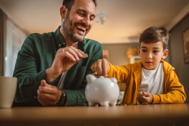 Baba ve oğul evdeki kumbarada birlikte para biriktiriyorlar.