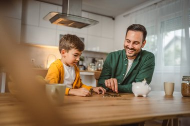 Baba ve oğul evdeki kumbarada birlikte para biriktiriyorlar.