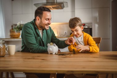 Baba ve oğul evdeki kumbarada birlikte para biriktiriyorlar.