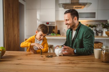 Baba ve oğul evdeki kumbarada birlikte para biriktiriyorlar.