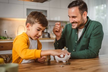 Baba ve oğul evdeki kumbarada birlikte para biriktiriyorlar.