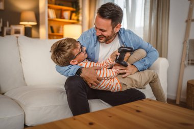 Yetişkin Kafkasyalı baba ve oğlu video oyunlarından sonra birbirlerine sarılıyorlar.