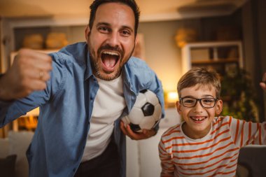 Evde futbol topunu neşelendiren bir baba ve oğulun portresi.