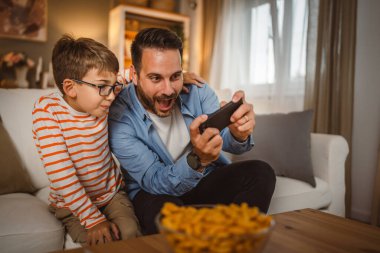 Baba ve oğul kanepede oturup evde cep telefonu kullanın. İyi eğlenceler.