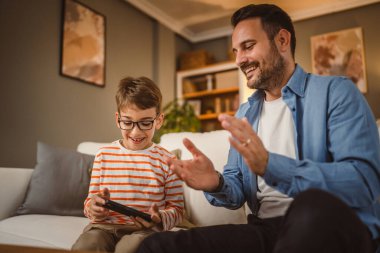 Baba ve oğul kanepede oturup evde cep telefonu kullanın. İyi eğlenceler.